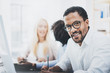 Dark skinned entrepreneur wearing glasses, working in modern office.African american man in white shirt looking and smiling at the camera.Horizontal,blurred background