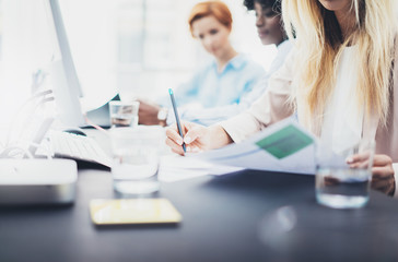 Closeup of young girls coworkers discussing together business project. Beautiful blonde woman signing documnet on workplace in office. Horizontal, blurred background.