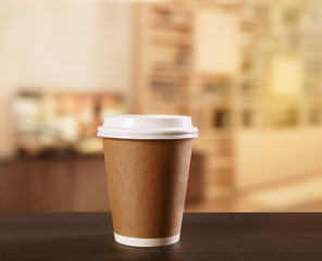 Poster - Paper cup of coffee on wooden table against blurred cafe interior background.