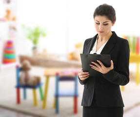 Canvas Print - Female teacher with clipboard on blurred playroom background