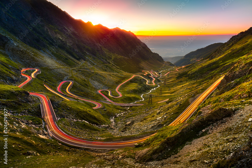 Traffic trails on Transfagarasan pass at sunset. Crossing Carpathian mountains in Romania, Transfagarasan is one of the most spectacular mountain roads in the world. - obrazy, fototapety, plakaty 