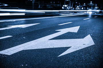 Nights lights of the big city, the night avenue with road markings and headlights of the approaching cars, close up view from asphalt level.