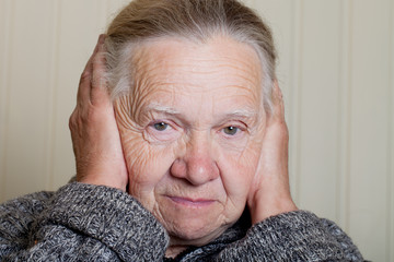 Portrait of an elderly woman with hands near face on a light bac