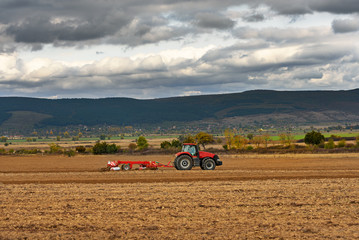 Fototapete - Tractor plowing a field at dusk