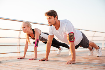 Young sports woman and man doing plank exercise together outdoors