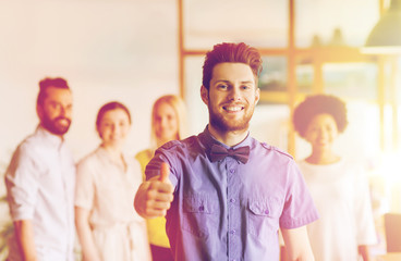 Canvas Print - happy man showing thumbs up over team in office