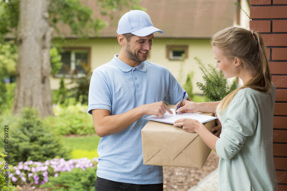 Courier holding a parcel and woman signing a delivery form - obrazy, fototapety, plakaty 