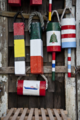 Colorful, abstract lobster bouys handing on an old rustic wooden shingled shed.