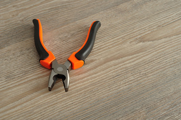 An orange and black pliers isolated on a wooden background