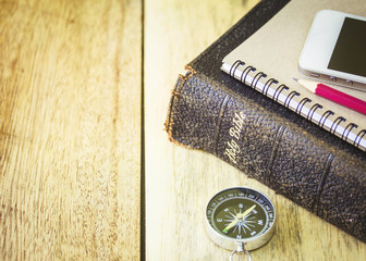 conceptual image of the compass  and holy bible  on with note book, pencil and mobile phone  over wooden background