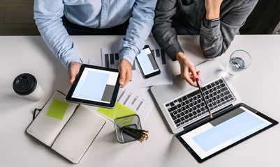 Top view of businessman and businesswoman sitting at white desk and do work together.Businesswoman showing pencil on laptop screen. Businessman using digital tablet.On table notebook,smartphone.