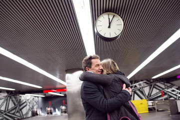 Wall Mural - Senior couple standing at the underground platform, hugging