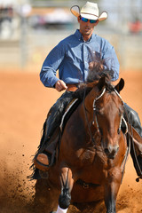 Wall Mural - The front view of a rider in cowboy chaps, boots and hat on a horseback running ahead and stopping the horse in the dust.