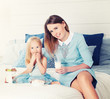 Mother and Daughter Sitting on the Bed, Eating Sweets and Drinki