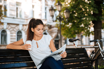 Woman reading newspaper while sitting on the bench