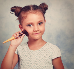 Cute beautiful small kid girl applying tonal cosmetic on the fac