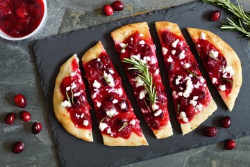 Wall Mural - Holiday flatbread appetizer with cranberries and goat cheese, overhead scene on a slate background