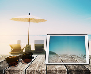 Wall Mural - The Beach Holidays, wooden table top, with digital tablet and sunglasses on blurred defocus blue sea and white sand beach in sunrise background