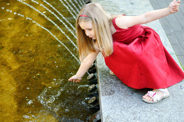 Wall Mural - Cute little girl playing with a city fountain on hot and sunny summer day