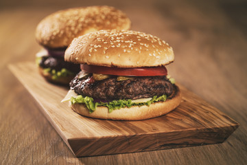 two homemade burgers on olive board on oak table