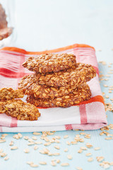 Homemade oatmeal banana cookies resting on napkin surrounded by oatmeal and blue wooden table