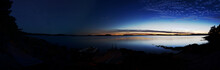 Panorama Of A Lake At Dusk And After Nightfall. On The Right Side Sky And Lake Are Illuminated By The Sunset. On The Left Side Stars Are Visible. The Foreground Is The Dark Silhouette Of The Coastline