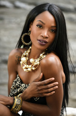Wall Mural - Exotic looking African American woman wearing black mini dress and jewellery with pearls posing sexy at outside location.