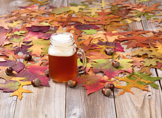 freshly poured beer with autumn foliage and acorns on wood