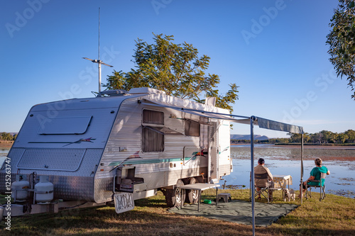 Fotomural Retired couple with small dog sitting enjoying view to lake alongside modern car