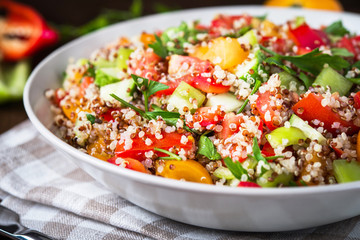 Fresh healthy salad with quinoa, colorful tomatoes, sweet pepper, cucumber and parsley on wooden background close up. Food and health. Superfood meal.