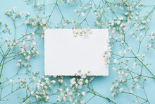 Wedding Mockup With White Paper List And Flowers Gypsophila On Blue Table From Above. Beautiful Floral Pattern. Flat Lay Style.