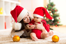Lovely Mother And Baby In Santa Red Dress Smile On A Background Of Christmas Trees In The Interior Of The House