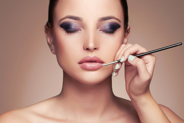 Wall Mural - beautiful woman face. beauty girl with perfect make-up.makeup artist applies lipstick.cosmetics
