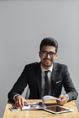 Handsome young businessman smiling and looking at camera in cafe while sitting against grey background