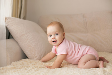 Wall Mural - Cute smiling baby in pink bodysuit on a beige couch