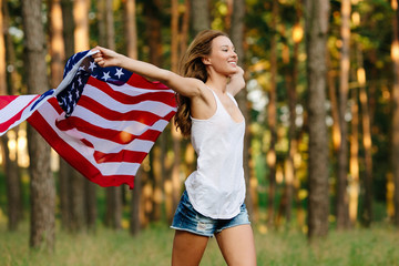 Girl in denim shorts running with American flag in hands.