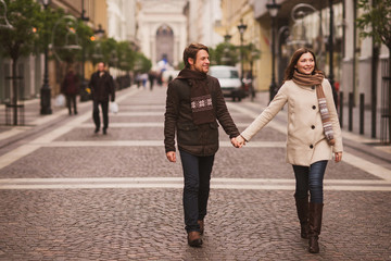 Canvas Print - Christmas in old town. Young cheerful caucasian couple in warm cozy clothes walking in city centre.