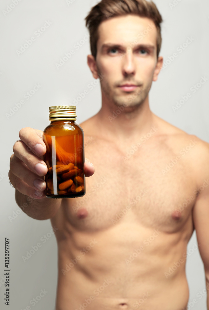 Muscular man holding drugs in bottle, closeup