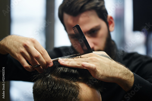 Cuadros en Lienzo El Barber un hombre con barba en el proceso de corte al cliente un par de tijera
