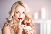 Smiling Blonde Woman With Big Curls Holding Creamy Cupcake With Strawberry On Top. Posing In Room Over Lights. Looking At Camera.