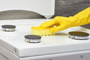 Hand in yellow glove cleaning white stove with sponge