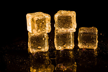 Ice cubes of gold color on a reflective surface.