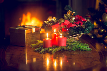 Wall Mural - Three burning candles and Christmas gift on table at fireplace