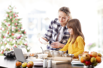 Wall Mural - Christmas time. Portrait of cute daughter and her mom baking christmas cookies together in the kitchen.