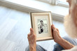 Elderly man holding photo frame with picture of young couple. Happy memories concept.
