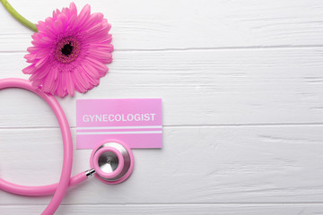 Business card with word GYNECOLOGIST, flower and stethoscope on white wooden background