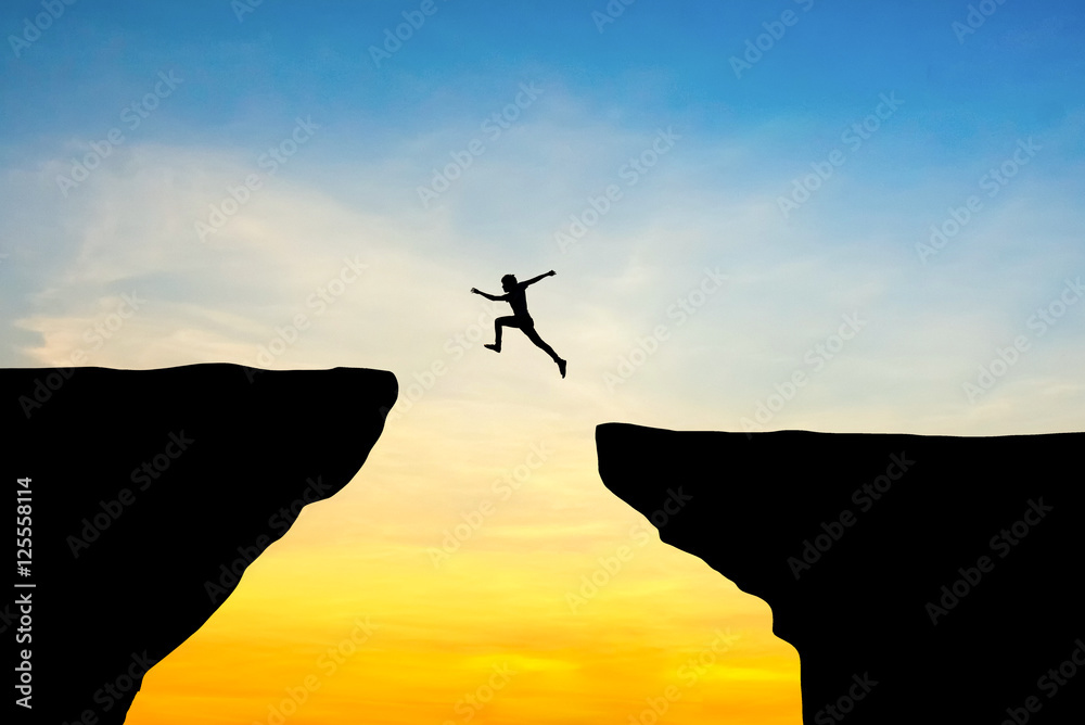 Man jump through the gap between hill.man jumping over cliff on sunset background,Business concept idea - obrazy, fototapety, plakaty 