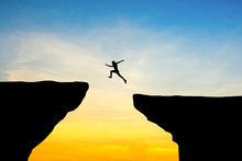 Man Jump Through The Gap Between Hill.man Jumping Over Cliff On Sunset Background,Business Concept Idea