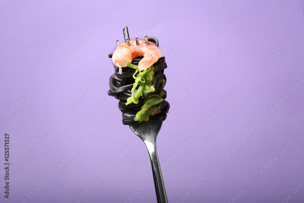 Fork with black pasta and shrimp on color background