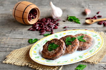 Wall Mural - Delicious bean burgers with garlic and spices on a plate. Small decorative barrel with raw red beans, garlic, parsley on an old wooden background. Vegetarian burgers. Rustic style